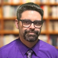 Headshot of director Eric Hansen in a purple dress shirt and tie